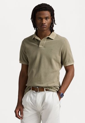 Polo de culoare verde măsliniu, cu o țesătură texturată, mâneci scurte și o deschidere cu două nasturi, asortat cu pantaloni albi și o curea maro.