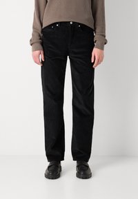 Black corduroy trousers with a straight cut, featuring a button and zipper closure, and side pockets. Worn with black shoes.