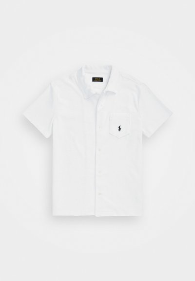 Λευκό πουκάμισο με κοντό μανίκι, φτιαγμένο από βαμβάκι, με τσέπη στο στήθος και μαύρο λογότυπο στην τσέπη, απαλό στην υφή.