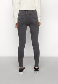 Jeans skinny grises de denim, con bolsillos traseros y una cintura alta. Combinados con zapatillas negras, mostrados desde atrás.