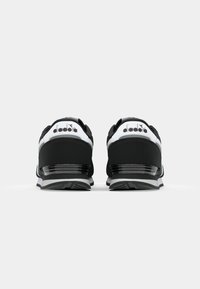 Black and white sneakers with a textured fabric upper, cushioned heel, and a sleek design. Features logo and contrasting accents.
