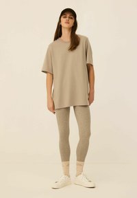 Beżowy, oversize'owy t-shirt, jasnoszare dopasowane legginsy i białe sneakersy. Model nosi ciemną czapkę; skarpetki z delikatnym tekstowym detalem.