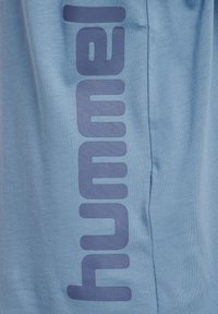 Ljusblå bomulls-t-shirt med ett stort, marinblått "hummel"-tryck på sidan. Tyget verkar mjukt med en slät textur.