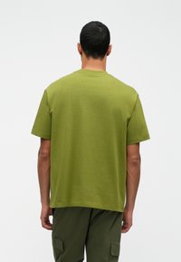 Zelena pamučna majica kratkih rukava, okruglog izreza i opuštenog kroja. Vidljivi šavovi duž rukava i donjeg ruba; teksturirana tkanina.