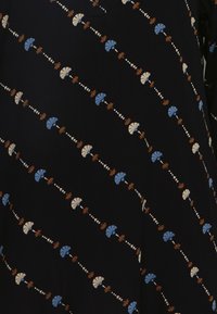 Tecido escuro com um padrão repetido de flores estilizadas em azul, branco e castanho, acentuado por pequenas formas brancas dispostas em diagonal.