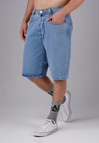Denim shorts in light blue, featuring a classic five-pocket design, mid-thigh length, and finished hem. Worn with gray socks and white sneakers.