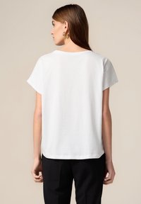 Weißes T-Shirt mit Rundhalsausschnitt und kurzen Ärmeln, mit lockerem Schnitt und leicht geschwungenem Saum, aus weichem Baumwollstoff gefertigt.
