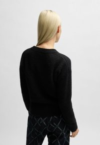 Maglione nero lavorato a maglia con finitura testurizzata, scollo rotondo e polsini a costine, abbinato a pantaloni scuri con motivo.