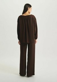 Ensemble bicolore marron comprenant un haut ample avec des manches volumineuses et un pantalon large, fabriqué à partir d'un tissu lisse et texturé.