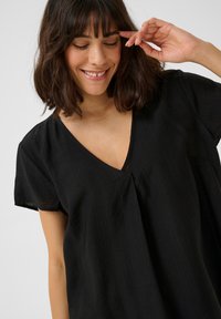 Black short-sleeve blouse with a V-neck, featuring a loose fit and subtle texture. Lightweight fabric creates a breathable design.