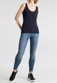 Canotta blu navy con scollo a barca, abbinata a jeans skinny azzurri con risvolti e scarpe sportive nere con suole bianche.