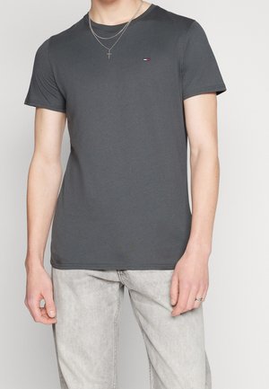 Graues Baumwoll-T-Shirt mit kurzen Ärmeln, rundem Halsausschnitt und kleinem gesticktem Logo auf der Brust. Kombiniert mit hellgrauen Jeans.