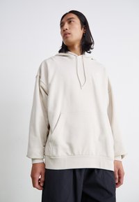 Haut de hoodie surdimensionné beige clair en tissu doux. Comprend une poche kangourou, une capuche avec cordon de serrage ajustable et des poignets côtelés.