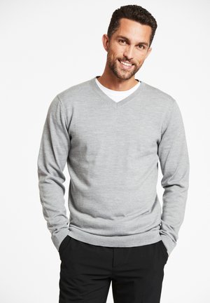 Grauer V-Ausschnitt-Pullover aus weichem Material, mit langen Ärmeln und lockerer Passform. Akzentuiert mit einem weißen Unterhemd darunter.