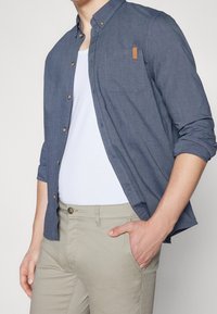 Marineblauwe button-up shirt van lichtgewicht stof, met een borstzak en een bruine leren label. Gepaard met lichtbeige chino's.