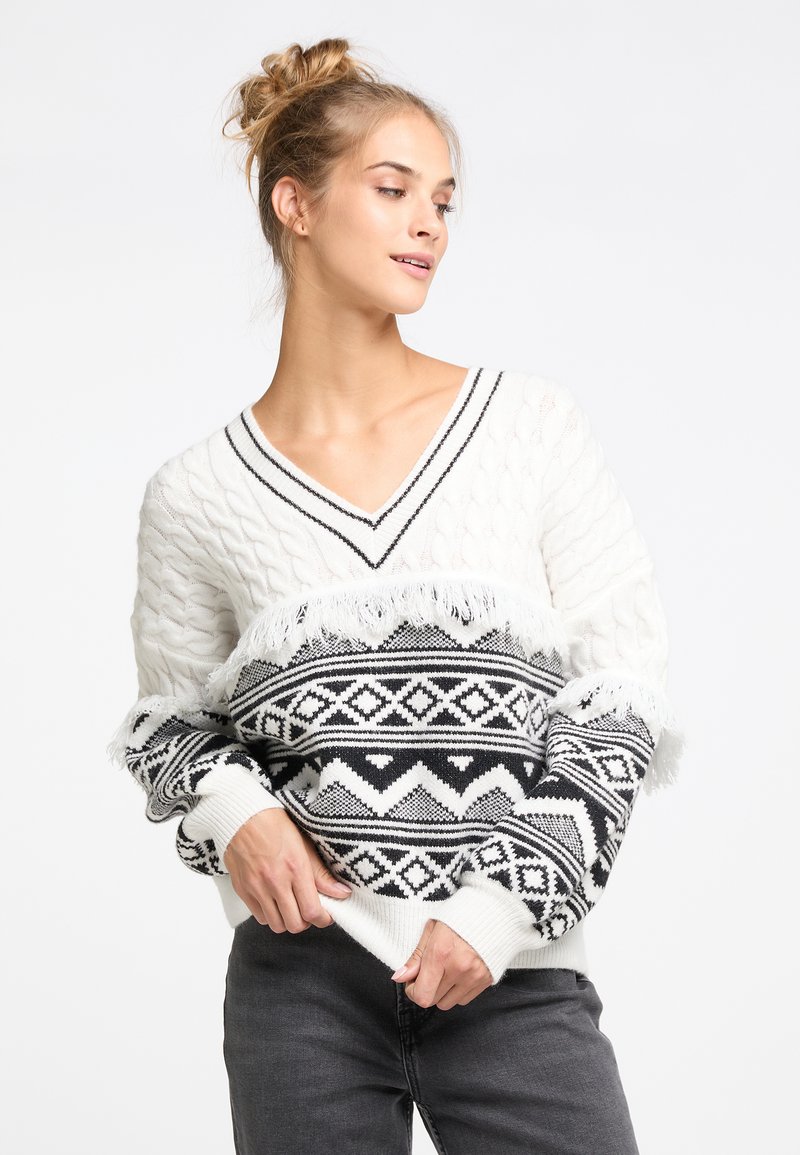 Weißer Strickpullover mit schwarzen geometrischen Mustern, V-Ausschnitt-Design und Fransenakzenten. Strukturierte Ärmel und eine gemütliche, lockere Passform.