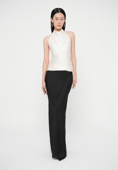 Biely top na zaväzovanie za krk s dramatickou látkou, v kombinácii s čiernou dlhou sukňou s bočným rázporkom. Hladké textúry a priliehavý strih.