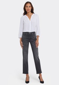 Vit blus med lång ärm, V-ringning och elastiska muddar, kombinerad med mörkgrå jeans med raka ben och svarta spetsiga klackskor.