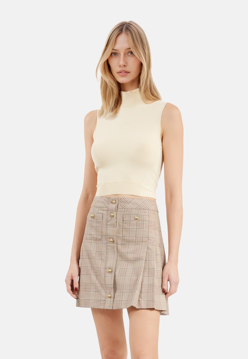 Top senza maniche color crema con collo alto abbinato a una mini gonna a scacchi beige con bottoni dorati e orlo svasato.
