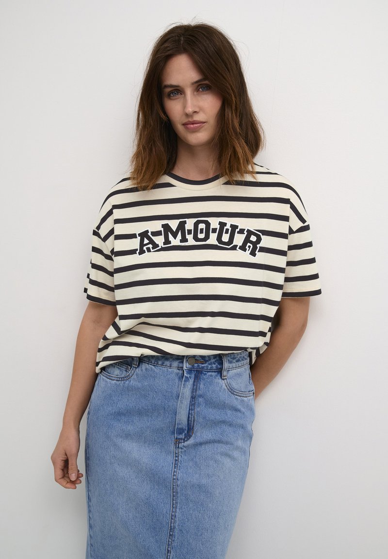 Gestreepte katoenen t-shirt in beige en marineblauw met een ronde halslijn en een relaxed fit; voorzien van de tekst "AMOUR" in vetgedrukt lettertype. Gecombineerd met een denim rok.