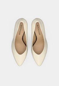 Δερμάτινες γόβες σε κρεμ απόχρωση με μυτερή μύτη και ομαλή υφή. Το εσωτερικό διαθέτει μπεζ επένδυση και διακριτικό λογότυπο.