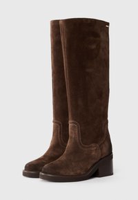 Bottes en daim marron montant jusqu'au genou avec un design incurvé, des accents cousus, un bout arrondi et un talon carré, mettant en valeur une texture douce.