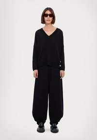 Maglione nero a collo a V con spalle scese e bottoni laterali abbinato a pantaloni neri larghi e scarpe nere chunky.