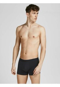 Schwarze Boxershorts mit einem weichen Bund, die eine enganliegende Passform, glatte Textur und einen horizontalen Eingriff aufweisen, getragen von einem männlichen Modell.