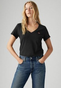 Camiseta negra de cuello en V hecha de algodón suave, con un pequeño logo rojo de Levi's en el pecho, combinada con jeans de denim azul de talle alto.