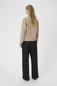 Beige stickad tröja med avslappnad passform, med rundad halsringning och ribbad nederkant. Matchad med vida svarta byxor.