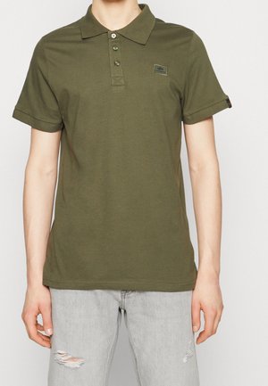 Olive green polo shirt in soft cotton with a collar, three buttons, and rolled short sleeves; features a small logo patch on the chest.