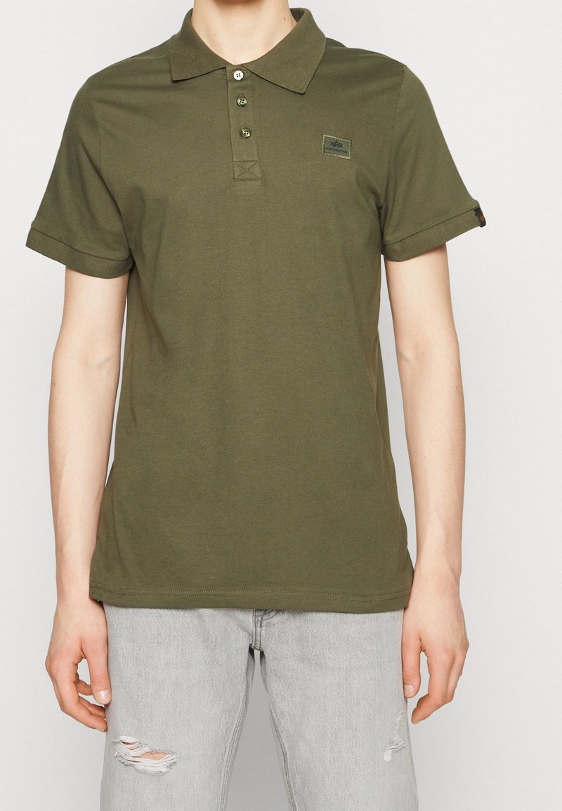 Olivově zelené polo tričko z měkké bavlny s límečkem, třemi knoflíky a ohrnutými krátkými rukávy; obsahuje malou nášivku loga na hrudi.
