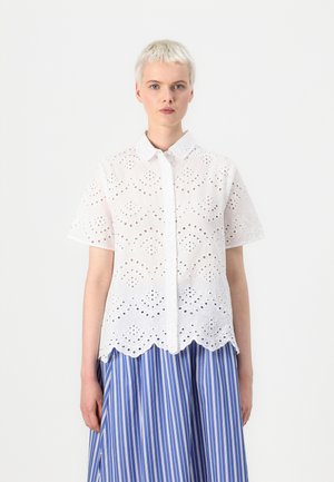 Hvit kortermet skjorte med brodert utskjæringsmønster, bølgekant og knappeåpning, kombinert med et blått og hvitt stripete skjørt.