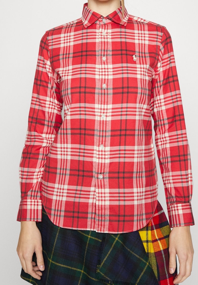 Röd rutig skjorta med vita och svarta detaljer, med krage som knäpps, långa ärmar och en diskret broderad logotyp på bröstet.