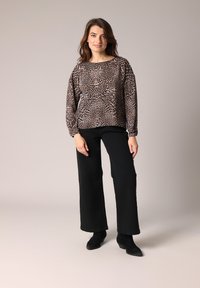 Haut à manches longues, imprimé léopard en beige et noir, associé à un pantalon large noir et des bottines. Tissu doux et coupe décontractée.