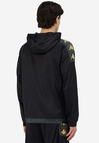 Felpa sportiva nera con cappuccio regolabile, vestibilità aderente, texture opaca e dettagli con il logo Kappa a fantasia sulle spalle.