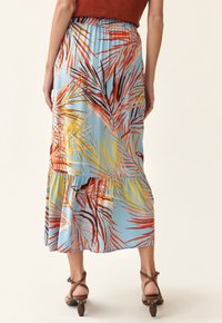 Jupe maxi avec une base bleue ornée de motifs de feuilles de palmier vibrants en orange, jaune et rouge. Taille élastique et design en étages.
