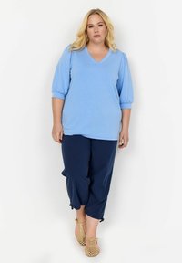 Világoskék, V nyakú blúz puffos ujjakkal, sötétkék, croppolt nadrággal párosítva. Puha textúrájú és laza szabású, világoskék cipőkkel kiegészítve.