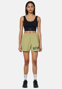 Schwarzes Crop-Top mit "HALO"-Logo, kombiniert mit hellgrünen Shorts mit "ATM"-Druck, elastischem Bund und schwarzen Sneakers.
