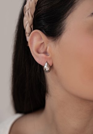 Silberne Tropfnach earrings mit einer glatten, polierten Oberfläche, hängend vom Ohrläppchen, das Licht reflektierend und seine aerodynamische Form zur Schau stellend.