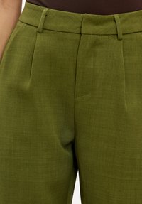 Pantalon vert en tissu texturé, avec une taille haute, des plis à l'avant et deux poches latérales pour plus de fonctionnalité.