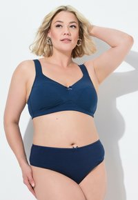 Donkerblauwe beha en hooghangende slip set in zachte, rekbare stof met een strikaccent op de beha en slip. Brede banden en naadloos ontwerp.