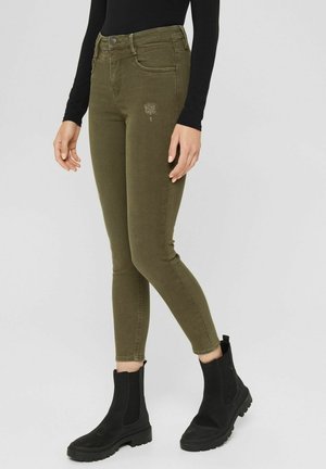 Oliven grønne skinny jeans med midt-lav talje, med knaplukning og diskret broderi foran, kombineret med sorte ankelstøvler.