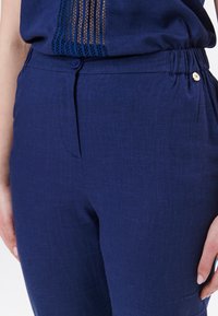 Navyblauwe linnen broek met een zachte textuur, voorzien van een knoopsluiting en een elastische tailleband voor een goede pasvorm. Subtiele stikdetails aanwezig.