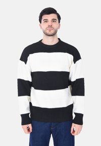 Maglione a righe bianche e nere in maglia con finitura testurizzata, collo a giro, maniche lunghe e ampie bande orizzontali.