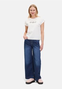 T-shirt blanc en coton avec des manches retroussées et des bulles de dialogue graphiques noires. Associé à un jean en denim bleu foncé à jambes larges, avec une coupe droite.
