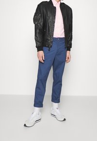 Czarna skórzana kurtka bomberka, jasnoróżowa koszula, niebieskie spodnie tapered oraz białe trampki z szarymi akcentami. Kurtka ma zapinane na zamek kieszenie.