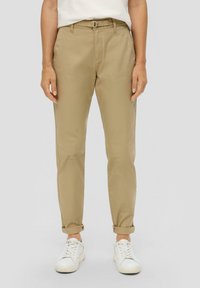 Khaki chinos met een zachte textuur, taps toelopende pijpen, riemlussen en opgerolde boorden. Gecombineerd met witte sneakers.