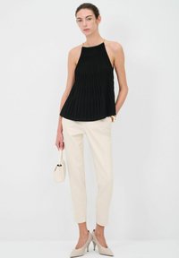 Zwarte geplooide top met een halternekontwerp, gecombineerd met crèmekleurige tailored broeken en beige hoge hakken. Minimalistische esthetiek.