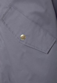 Gray fabric with a smooth texture features a flap pocket secured by a shiny brass button, complemented by precise stitching along the edges.